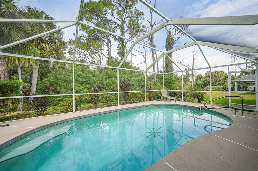 A swimming pool enclosed by a white metal screen structure surrounded by lush green trees — 5379 ENSLEY TERRACE, NORTH PORT, FL