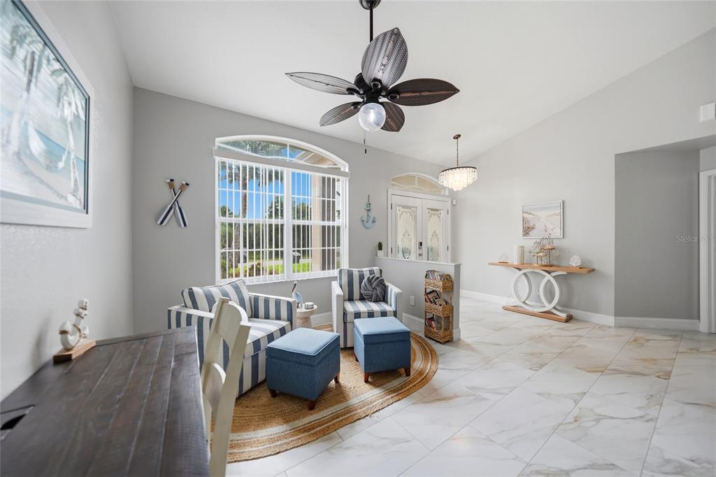 A bright living area features striped armchairs, blue ottomans, a ceiling fan, and tiled floors — 5379 ENSLEY TERRACE, NORTH PORT, FL