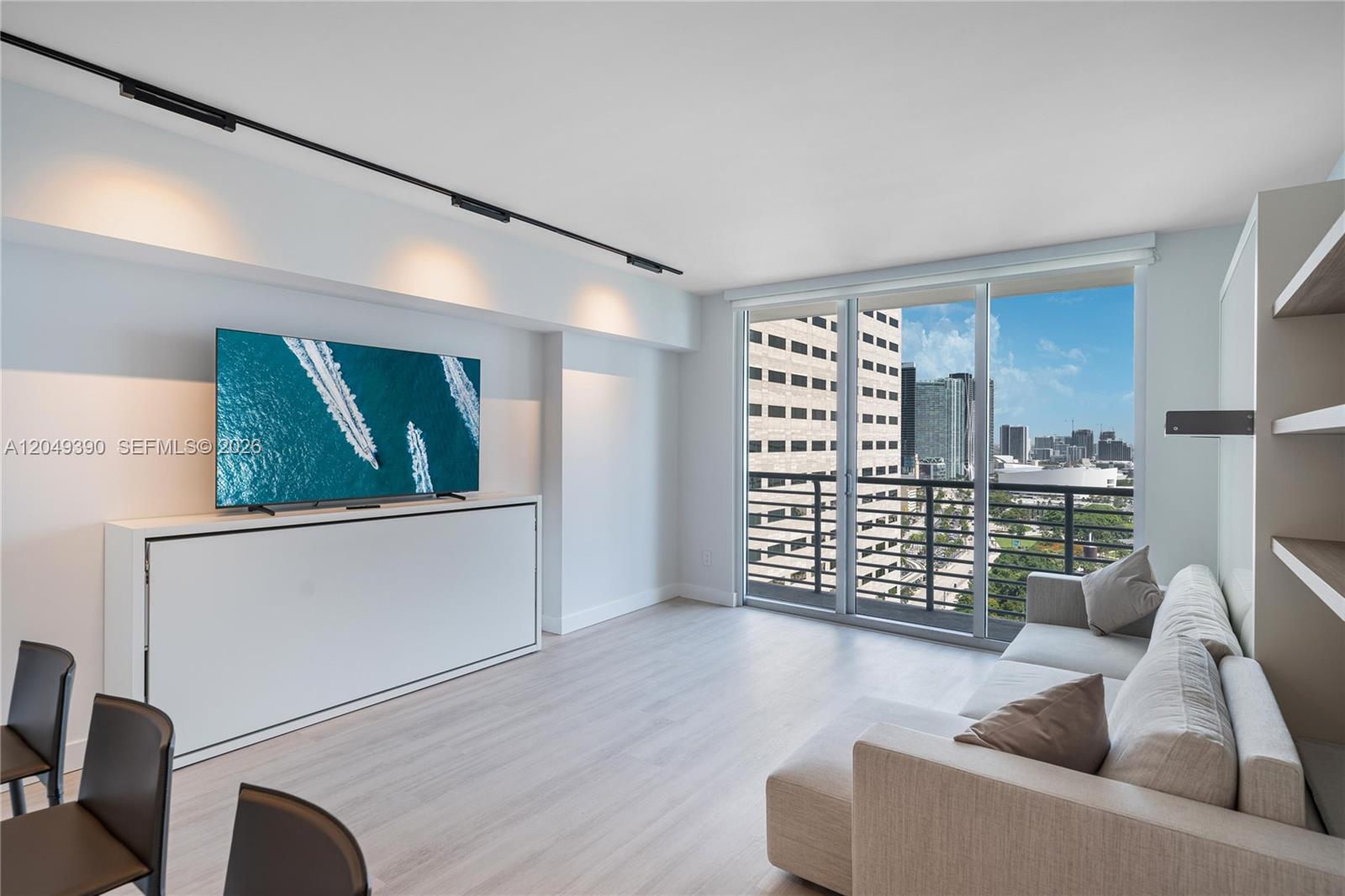 A modern living room features a wall-mounted television, a sofa, and floor-to-ceiling windows — 325 S Biscayne Blvd # 2920, Miami FL 33131, MIAMI, FL