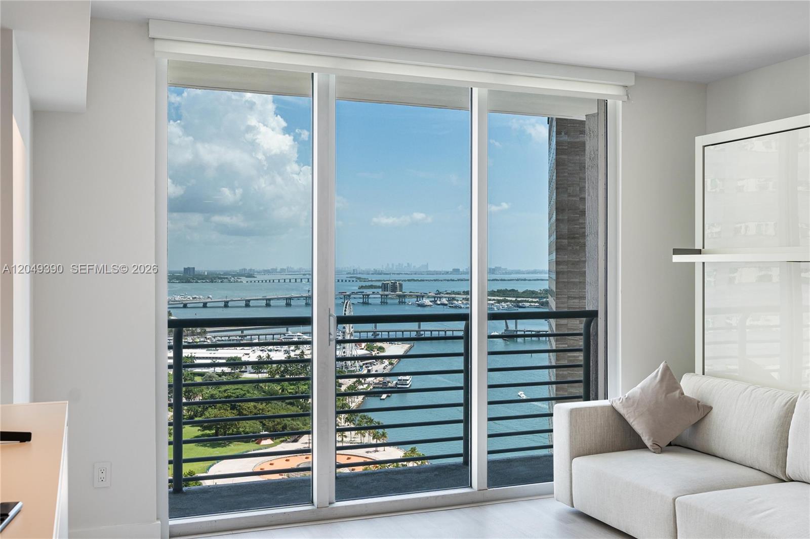 A room with a sofa and a balcony overlooking a bay with bridges — 325 S Biscayne Blvd # 2920, Miami FL 33131, MIAMI, FL