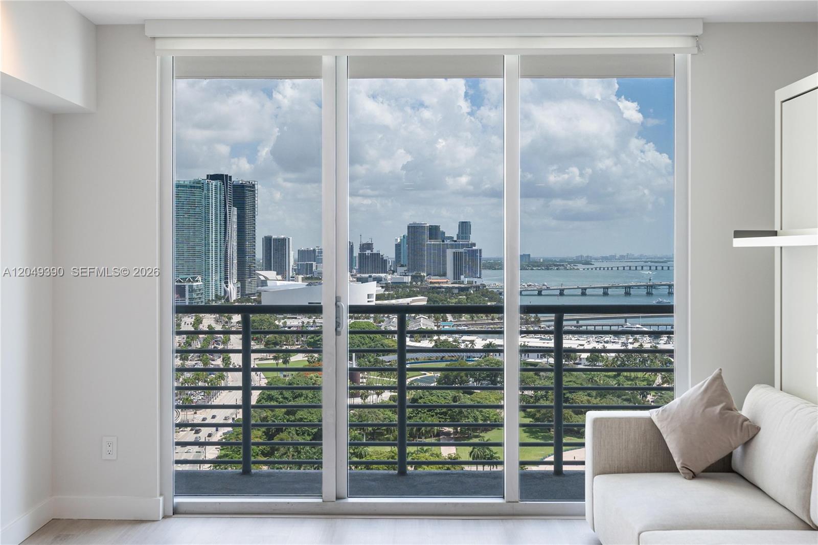 A living room features a large glass sliding door overlooking a city skyline and bay — 325 S Biscayne Blvd # 2920, Miami FL 33131, MIAMI, FL