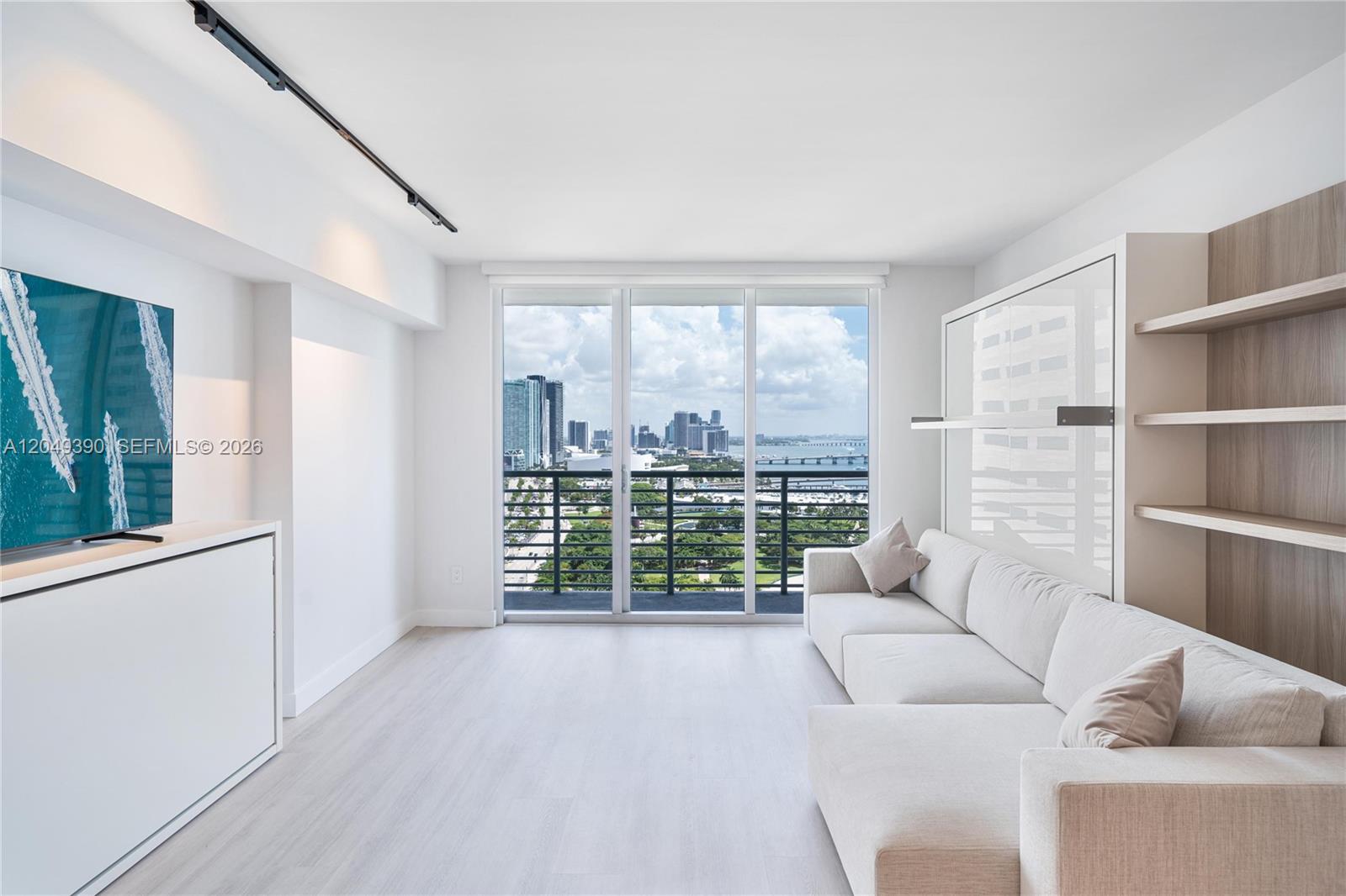 A modern living room features a white sofa, a wall bed, and a city view — 325 S Biscayne Blvd # 2920, Miami FL 33131, MIAMI, FL