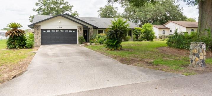 A single-story house with a dark garage door, stone accents, and a concrete driveway — 7213 REGENT DRIVE, LAKELAND, FL