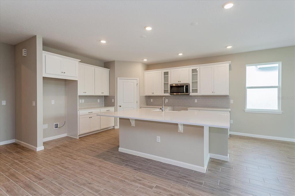 A kitchen with white cabinets, a large island, and light-colored wood-look tile flooring — 2240 AXEL STREET, MINNEOLA, FL