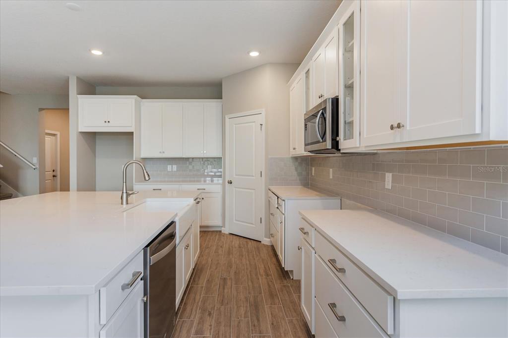 A modern kitchen features white cabinetry, quartz countertops, a large island, and gray subway tile — 2240 AXEL STREET, MINNEOLA, FL