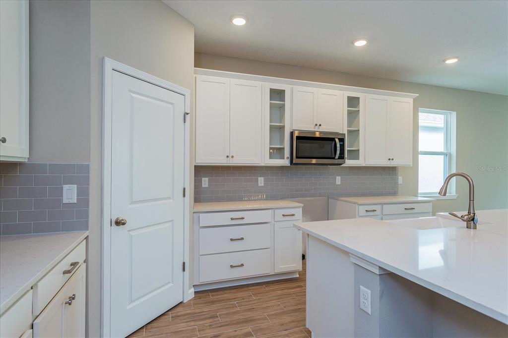 A kitchen features white cabinets, gray subway tile backsplash, quartz countertops, and a center island — 2240 AXEL STREET, MINNEOLA, FL