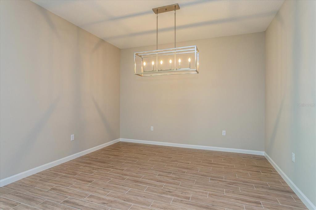 An empty room features light-colored walls, wood-look tile flooring, and a rectangular metal chandelier — 2240 AXEL STREET, MINNEOLA, FL