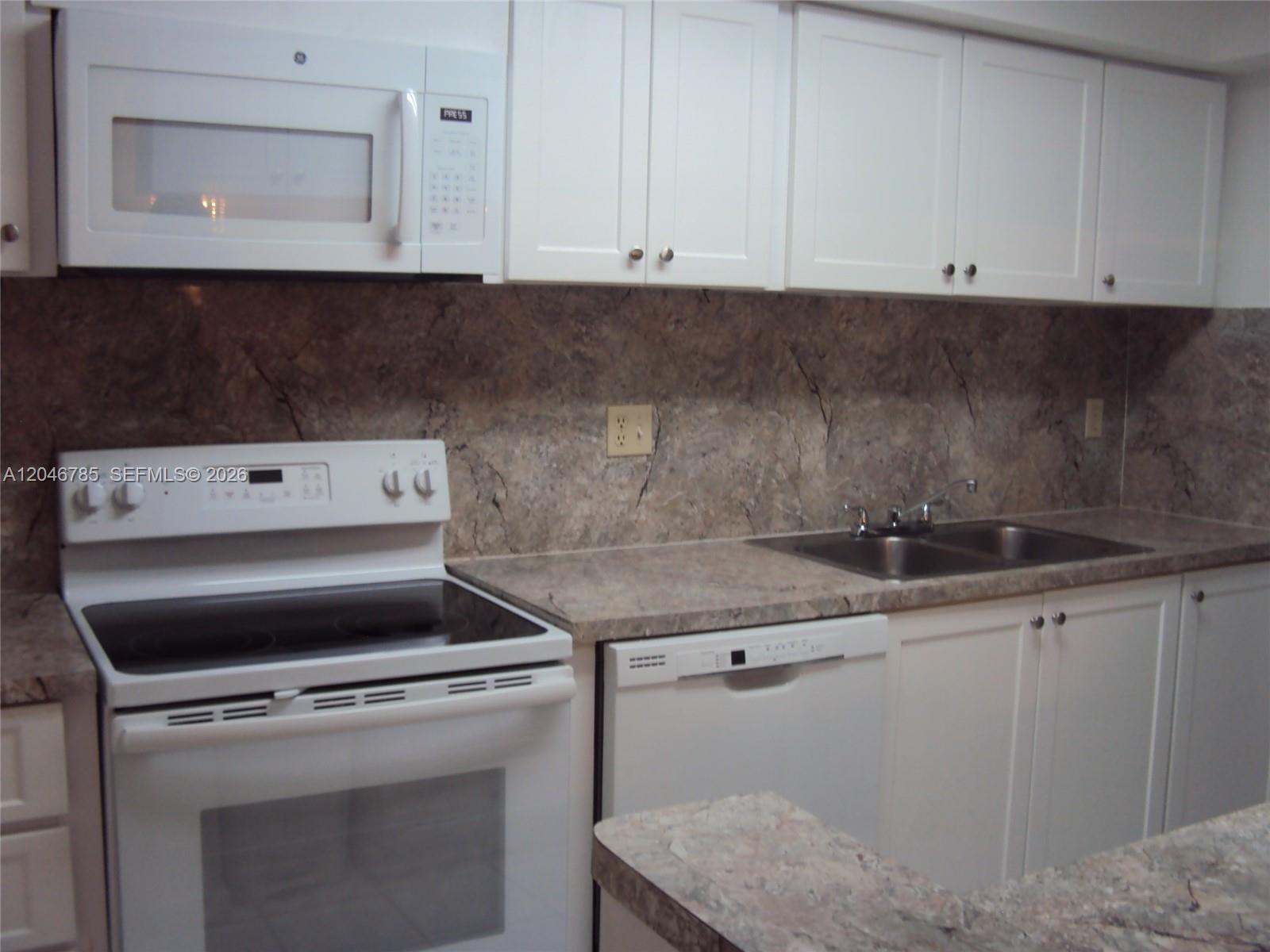 A kitchen features white cabinets, white appliances, and a brown marble-patterned countertop and backsplash — 8401 SW 107th Ave # 247E, Miami FL 33173, MIAMI, FL