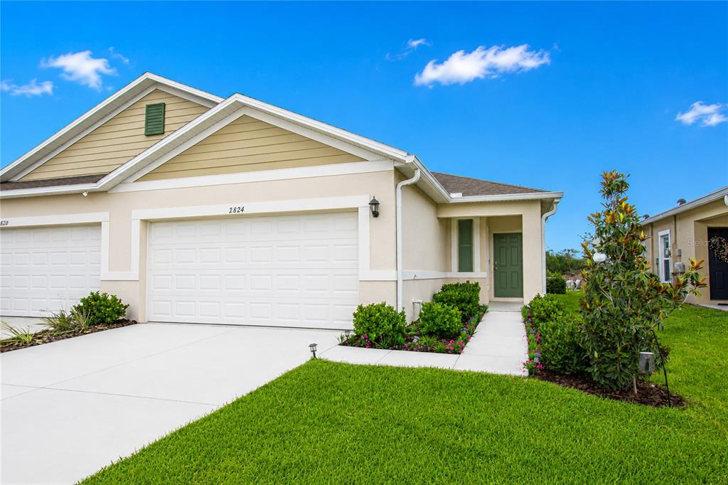 A single-story suburban home with a white garage, tan siding, and a green front door — 2824 SUNRIDGE LOOP, ST CLOUD, FL