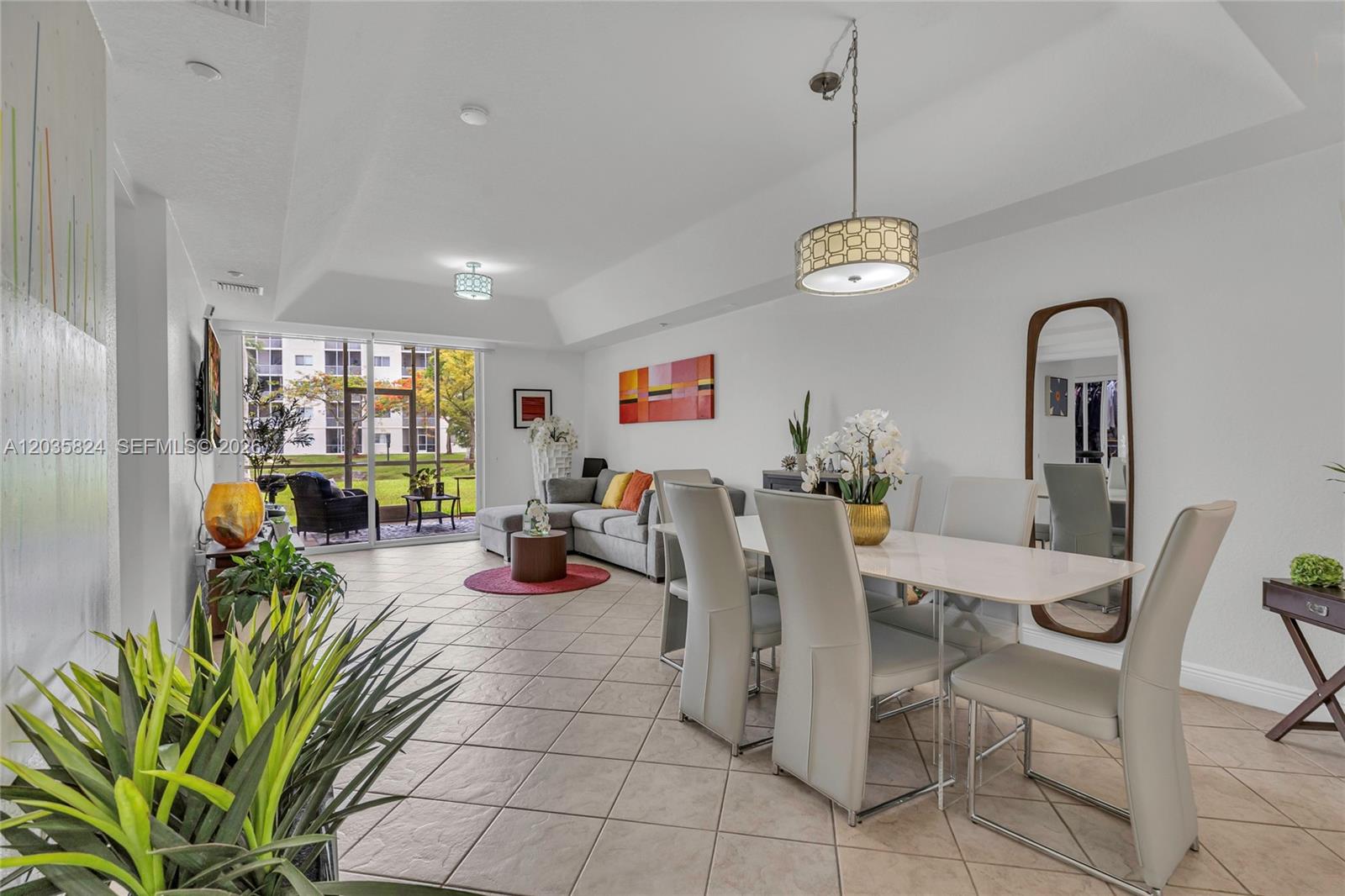 A bright open-concept living and dining area features tile floors, a tray ceiling, and patio access — 10710 NW 66th St # 104, Doral FL 33178, DORAL, FL