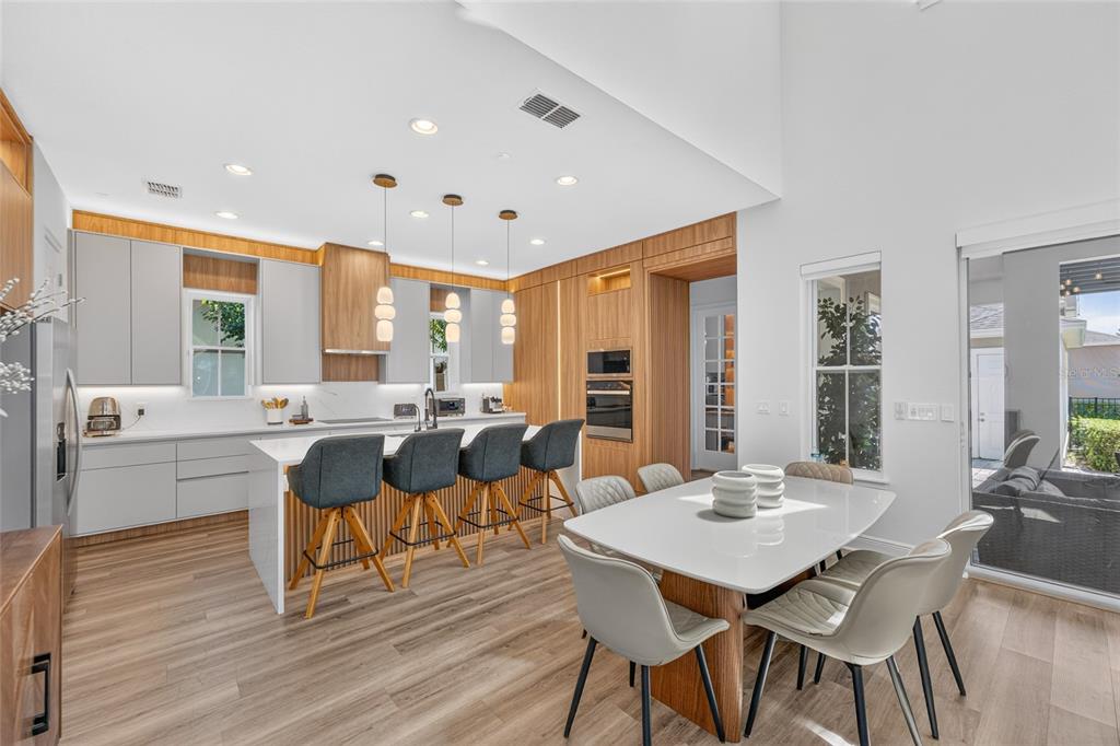 A modern kitchen and dining area features light wood cabinetry, white countertops, and gray seating — 13660 CHAUVIN AVENUE, ORLANDO, FL