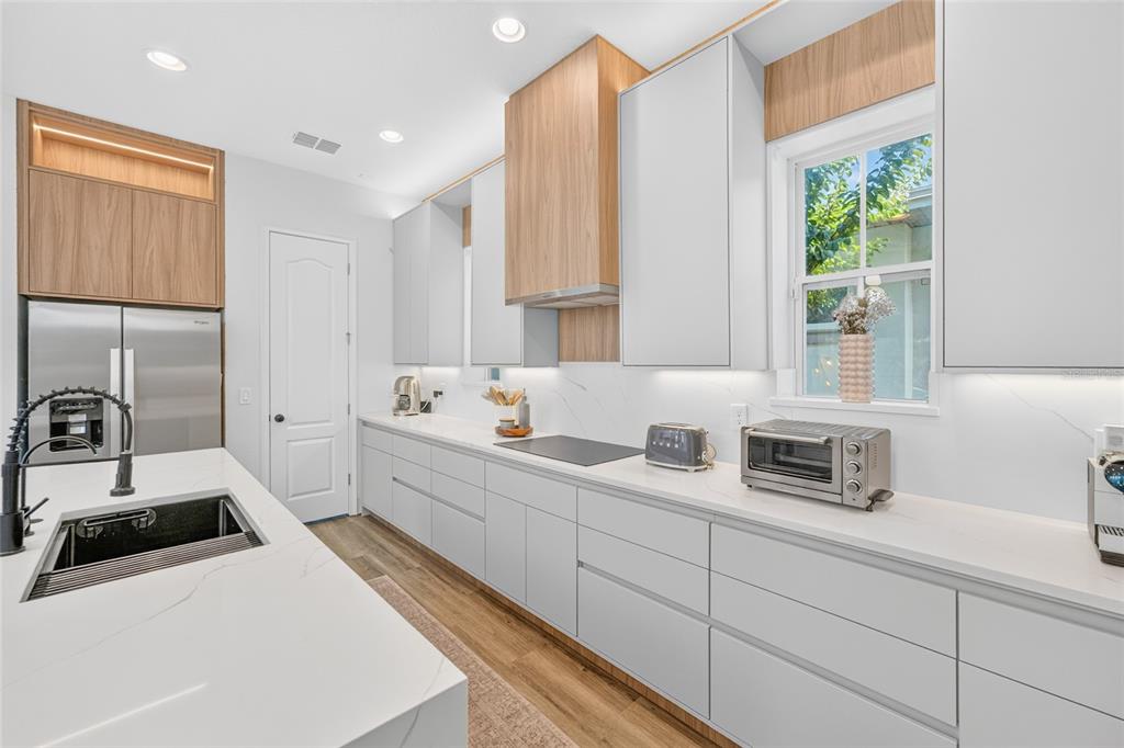 A modern kitchen features white cabinets, wood accents, a marble island, and stainless steel appliances — 13660 CHAUVIN AVENUE, ORLANDO, FL