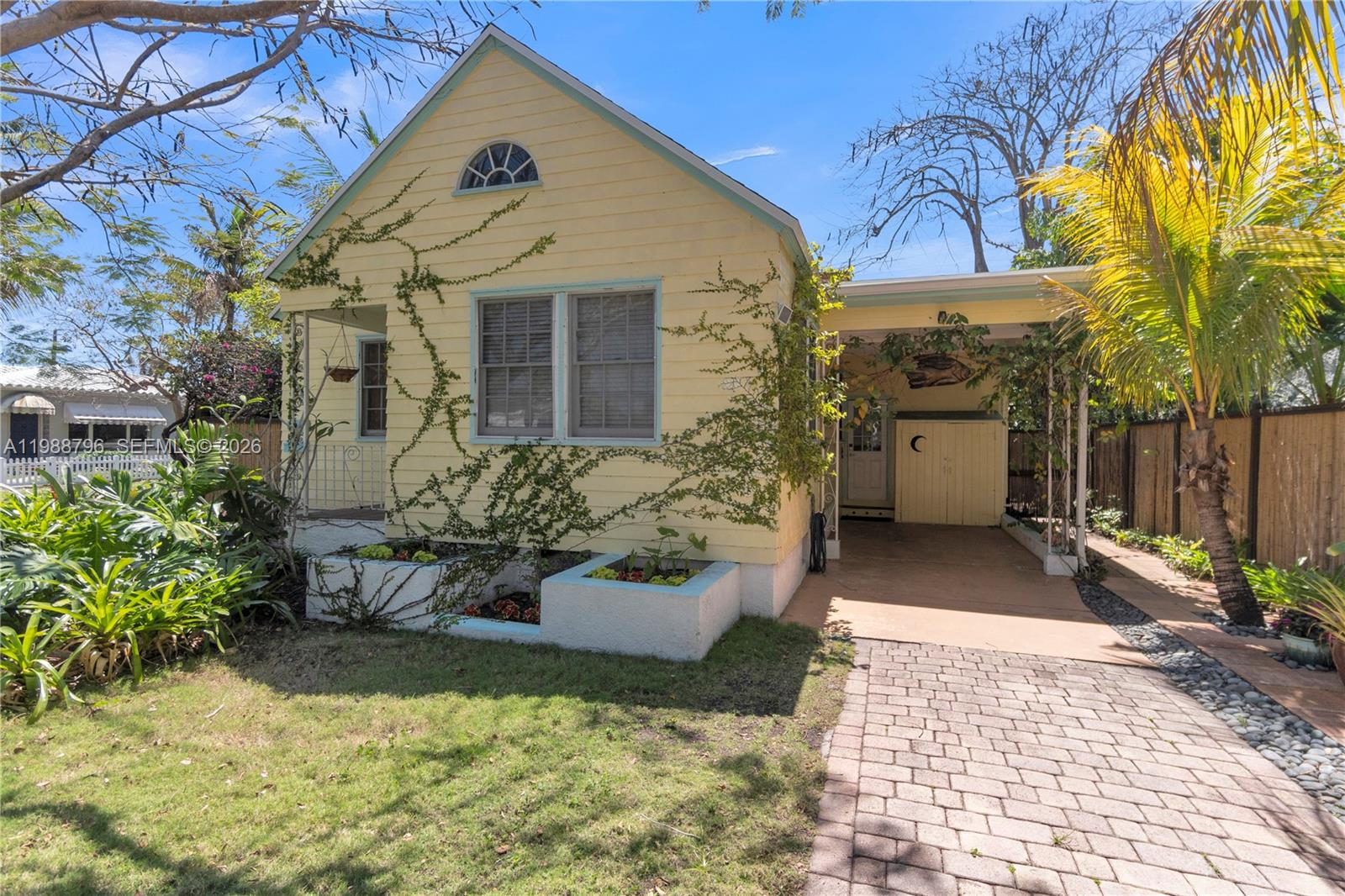 A yellow cottage with a carport, front porch, and brick driveway under a blue sky — 1500 Jackson St, Hollywood FL 33020, HOLLYWOOD, FL