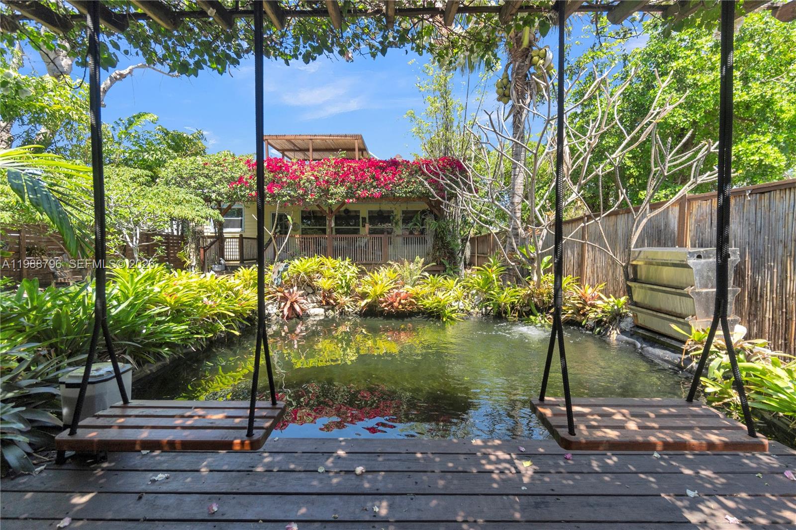 A wooden deck with two hanging swings overlooks a pond and a lush garden — 1500 Jackson St, Hollywood FL 33020, HOLLYWOOD, FL