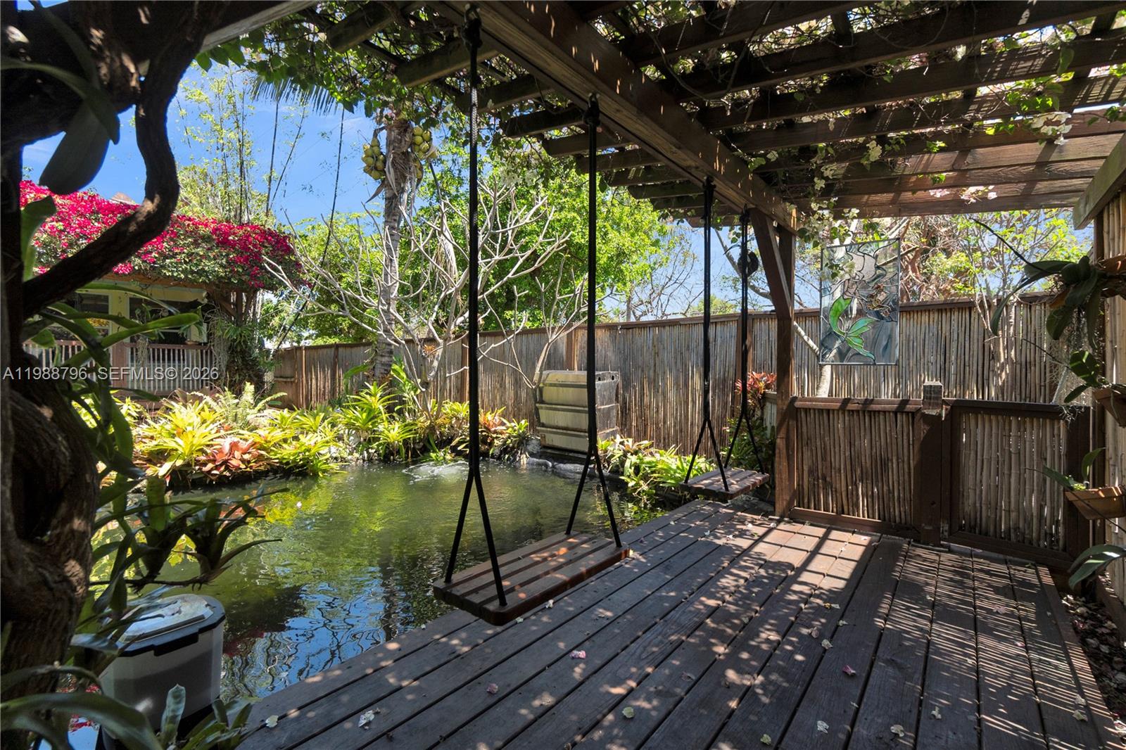 A wooden deck features two hanging swings overlooking a pond in a lush garden setting — 1500 Jackson St, Hollywood FL 33020, HOLLYWOOD, FL