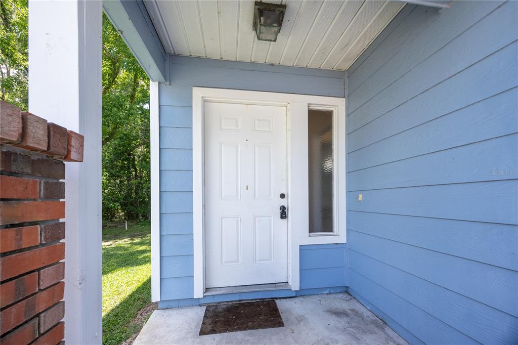 A white front door with a sidelight is set against blue horizontal siding — 218 NW 50TH BOULEVARD UNIT K, GAINESVILLE, FL