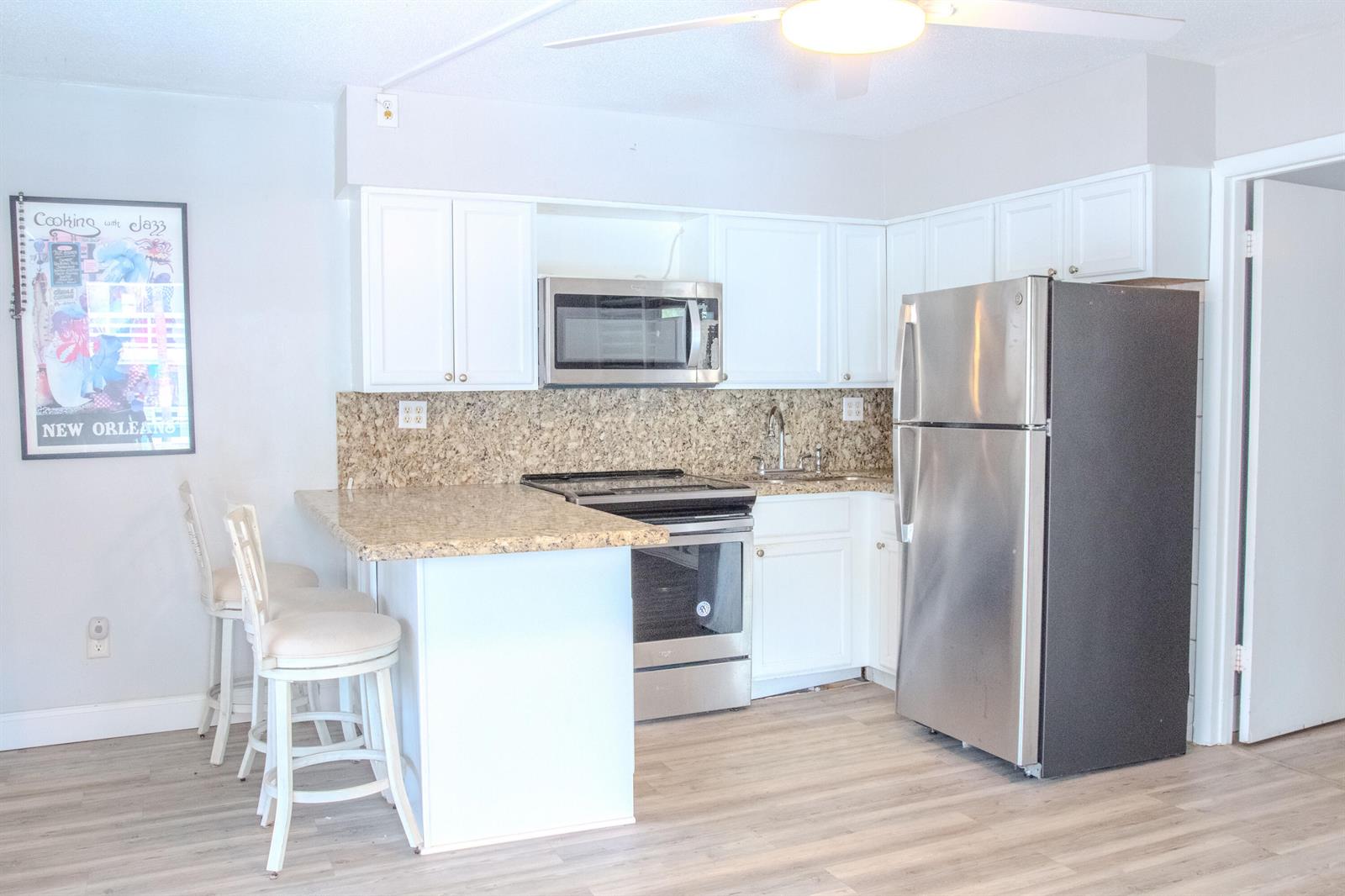 A kitchen features white cabinets, granite countertops, stainless steel appliances, and two bar stools — 11000 S Ocean Drive # 12, Jensen Beach FL 34957, JENSEN BEACH, FL