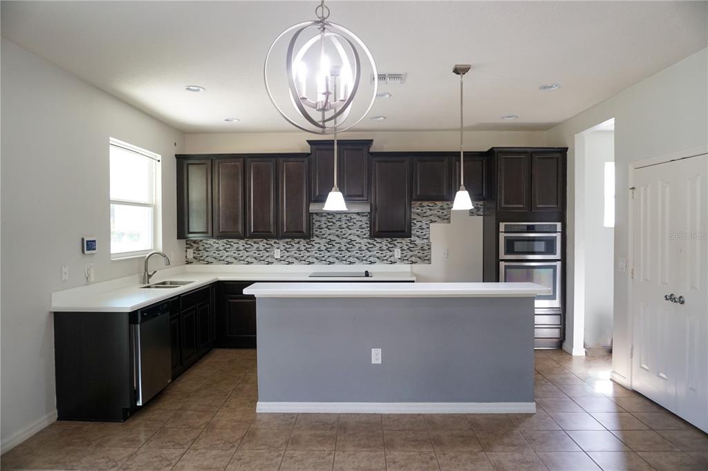 A kitchen features dark wood cabinets, white countertops, a gray island, and tile flooring — 2936 BOATING BOULEVARD, KISSIMMEE, FL