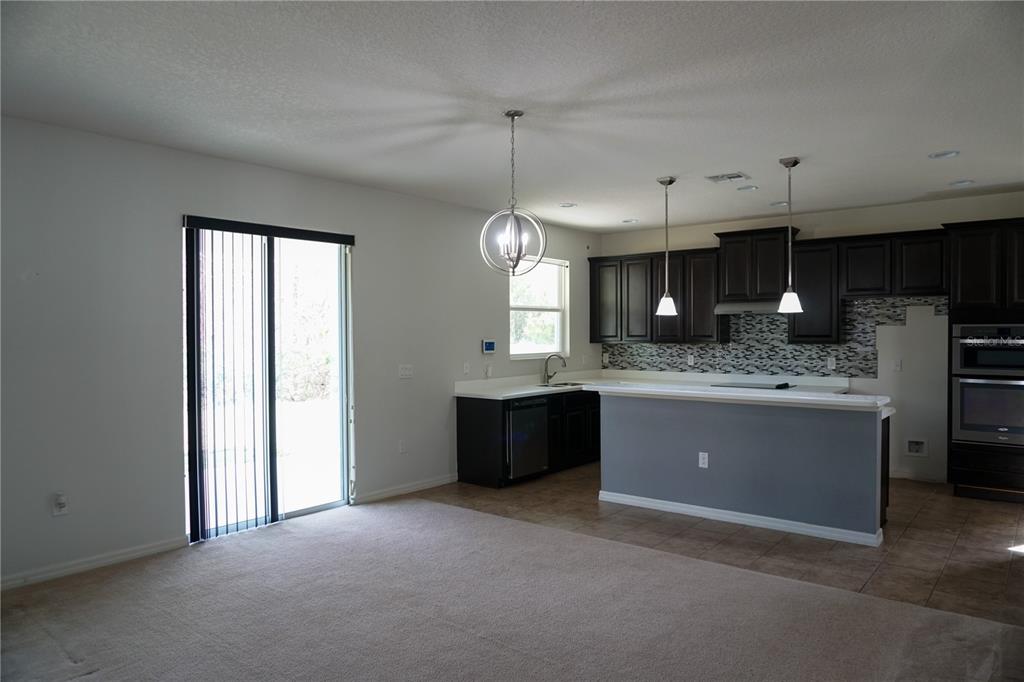 An open-concept kitchen with dark cabinets, a gray island, and a carpeted living area — 2936 BOATING BOULEVARD, KISSIMMEE, FL