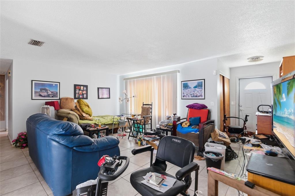 A living room with tile flooring, a blue sofa, a mobility scooter, and a television — 915 MARTIN LUTHER KING BOULEVARD NE, WINTER HAVEN, FL