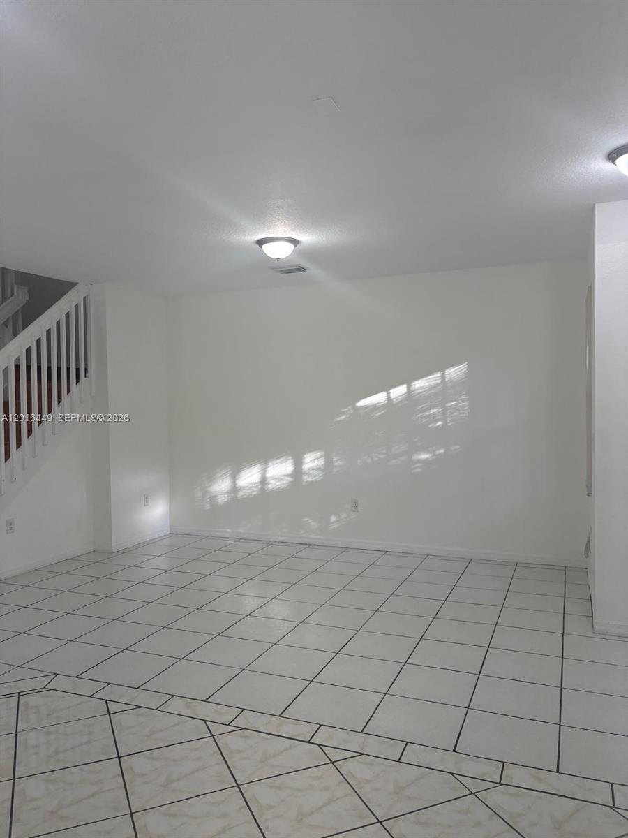 An empty room features white walls, a staircase with a white railing, and tiled flooring — 8525 SW 165th Pl # 8525, Miami FL 33193, MIAMI, FL