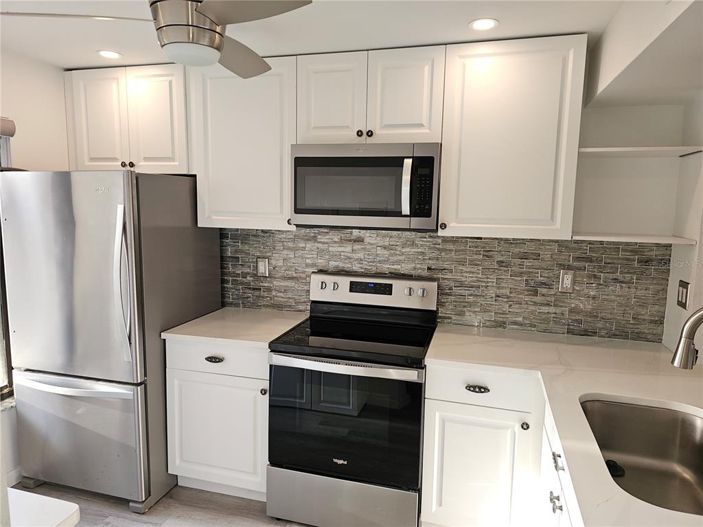 A kitchen features white cabinets, stainless steel appliances, a tiled backsplash, and light countertops — 6343 PALMA DEL MAR BOULEVARD S UNIT 126, ST PETERSBURG, FL