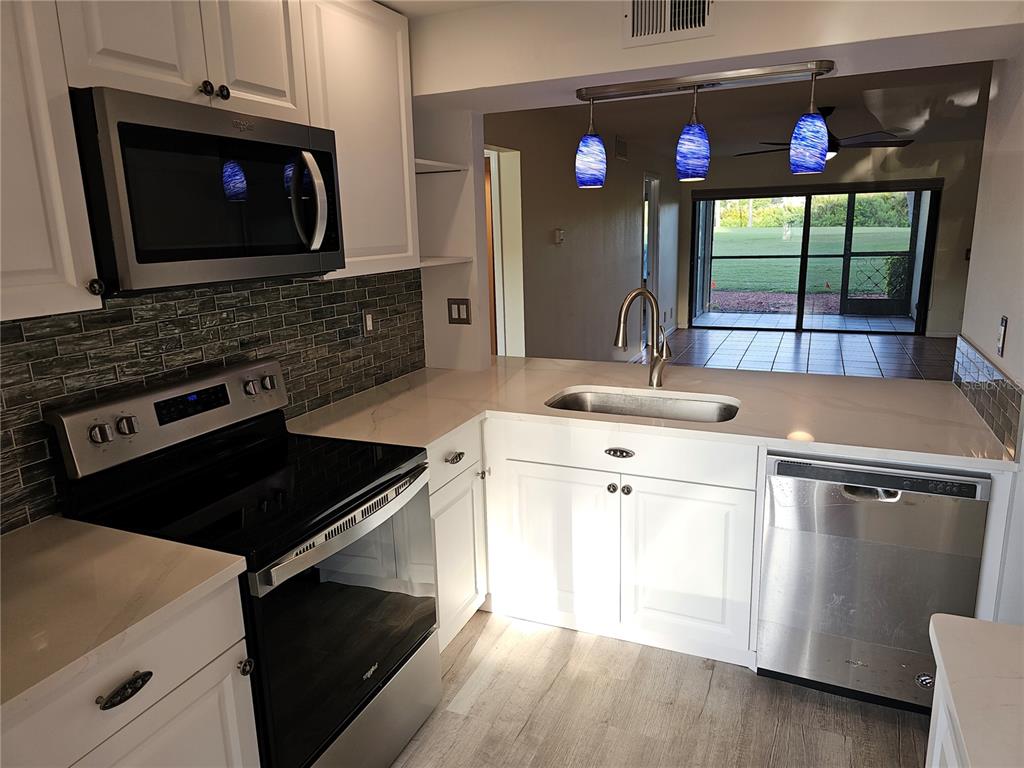 A kitchen features white cabinets, stainless steel appliances, a tiled backsplash, and a sink island — 6343 PALMA DEL MAR BOULEVARD S UNIT 126, ST PETERSBURG, FL