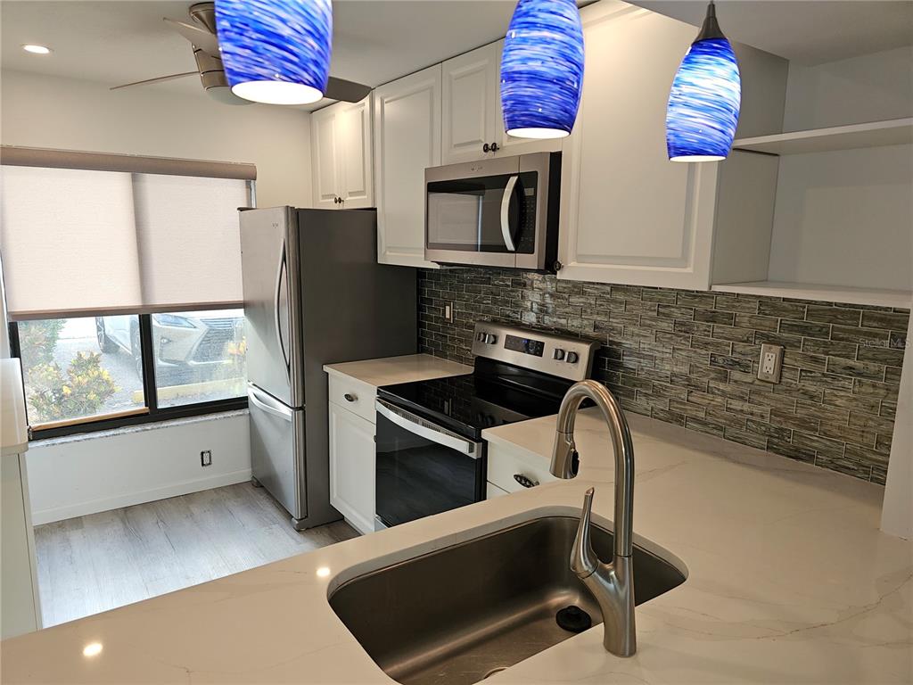 A kitchen features white cabinets, stainless steel appliances, a tiled backsplash, and a sink island — 6343 PALMA DEL MAR BOULEVARD S UNIT 126, ST PETERSBURG, FL
