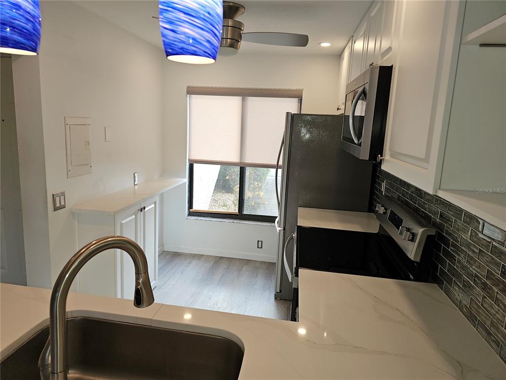 A kitchen features white cabinets, quartz countertops, a stainless steel refrigerator, and blue pendant lights — 6343 PALMA DEL MAR BOULEVARD S UNIT 126, ST PETERSBURG, FL