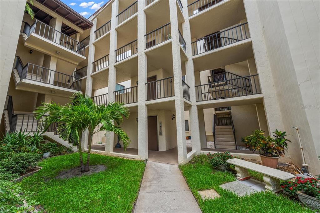 A multi-story apartment building exterior features open-air walkways, staircases, and a landscaped courtyard — 700 STARKEY ROAD UNIT 624, LARGO, FL