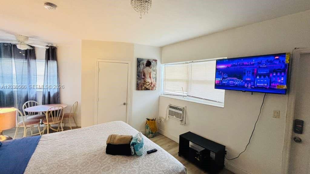 A bedroom features a bed, a wall-mounted television, a dining set, and a window unit — 109 SE 9th St # 2, Hallandale Beach FL 33009, HALLANDALE BEACH, FL