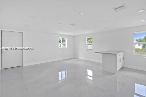 A bright, empty room with white walls, glossy tile floors, and a small kitchen island — 655 SW 5th St, Homestead FL 33030, HOMESTEAD, FL