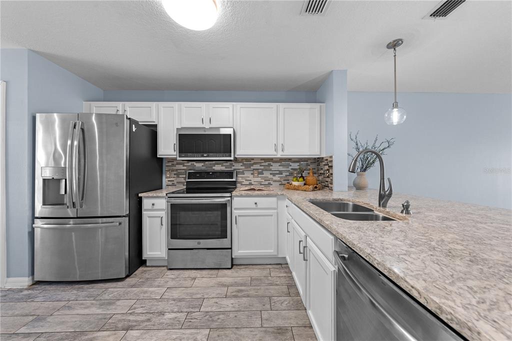 A kitchen features white cabinets, stainless steel appliances, granite countertops, and wood-look tile flooring — 2705 EMERALD LAKE CT UNIT 2705, KISSIMMEE, FL