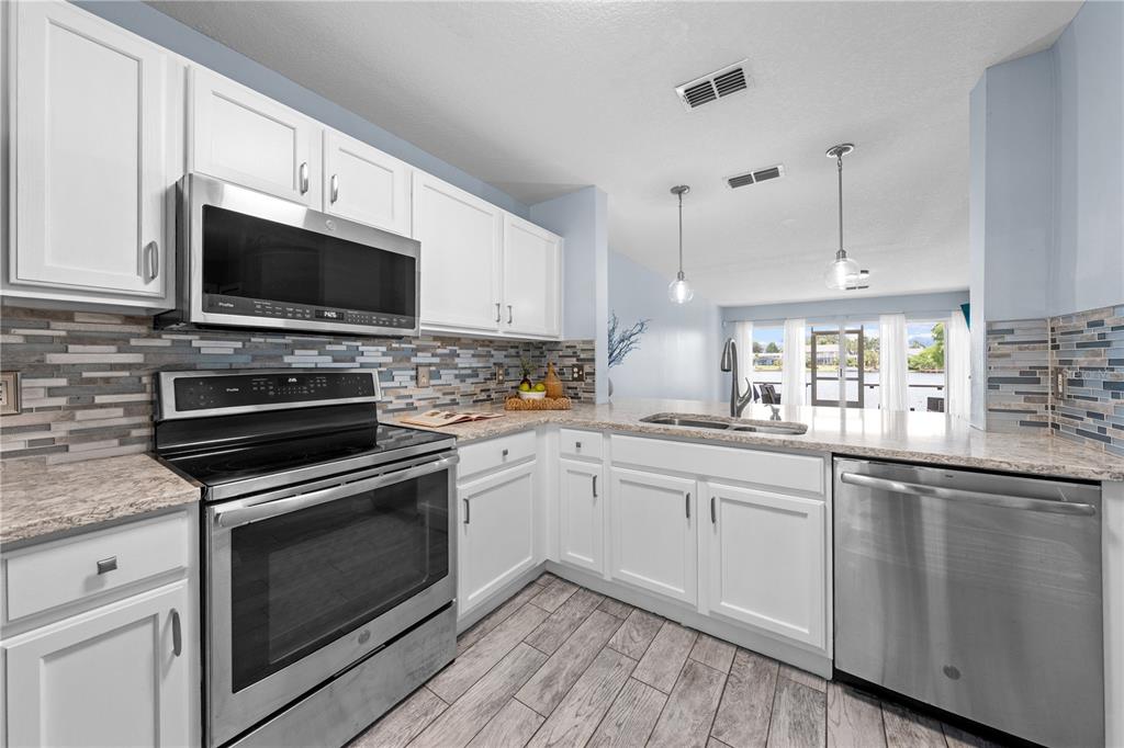 A kitchen features white cabinets, stainless steel appliances, a tiled backsplash, and wood-look tile flooring — 2705 EMERALD LAKE CT UNIT 2705, KISSIMMEE, FL