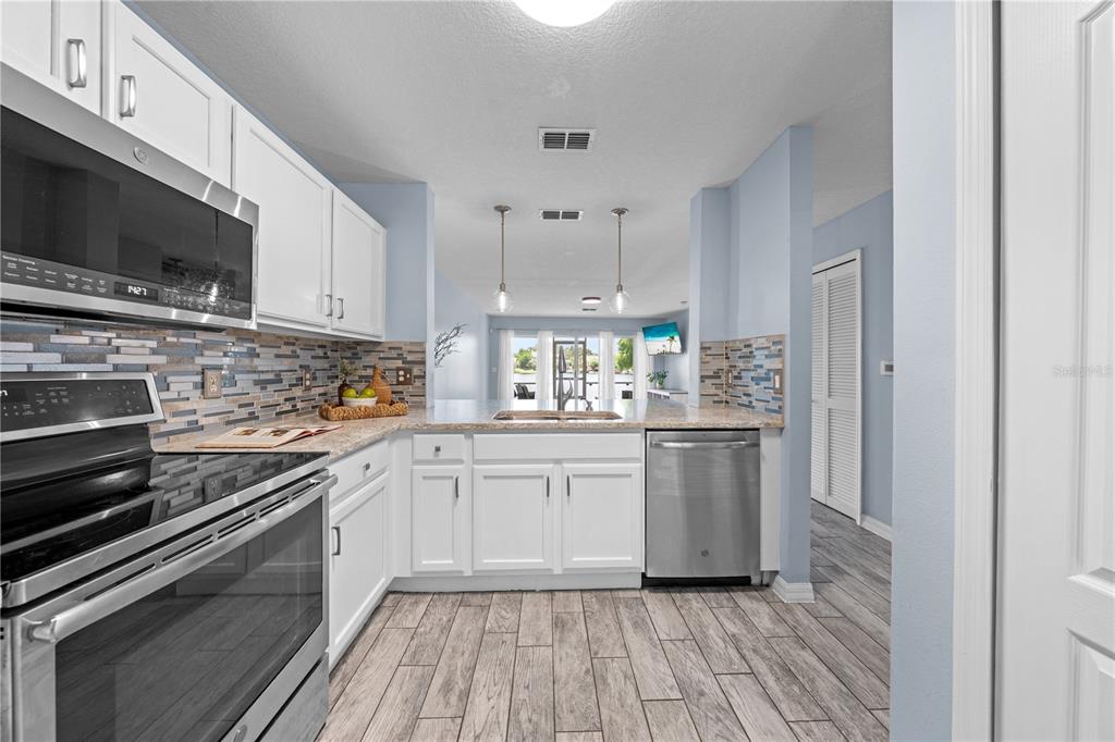 A kitchen with white cabinets, stainless steel appliances, and a tiled backsplash overlooks a living area — 2705 EMERALD LAKE CT UNIT 2705, KISSIMMEE, FL