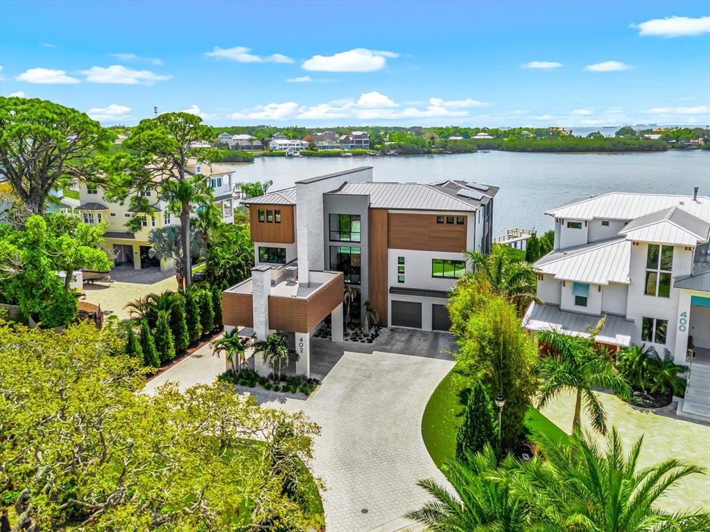A modern multi-story house with a white stone facade, wood paneling, and a paved driveway — 402 HILLSBOROUGH STREET, PALM HARBOR, FL