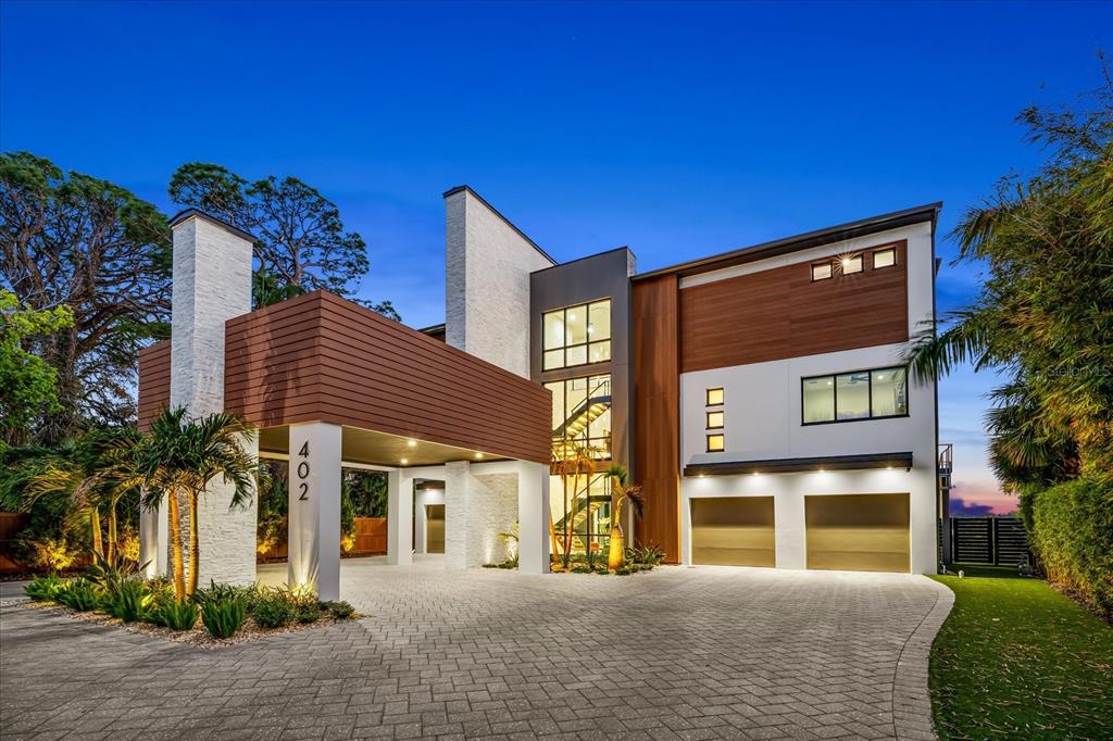 A modern multi-story house with a paved driveway, two-car garage, and wood-paneled exterior accents — 402 HILLSBOROUGH STREET, PALM HARBOR, FL
