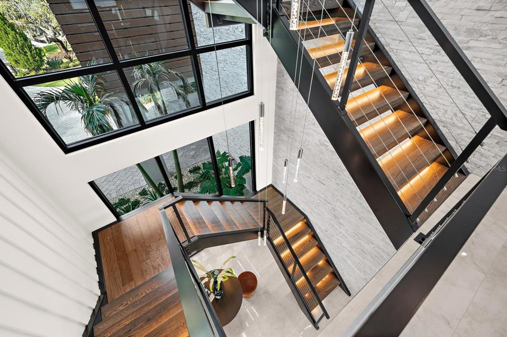A modern staircase with wood treads and metal railings overlooks a foyer with large windows — 402 HILLSBOROUGH STREET, PALM HARBOR, FL
