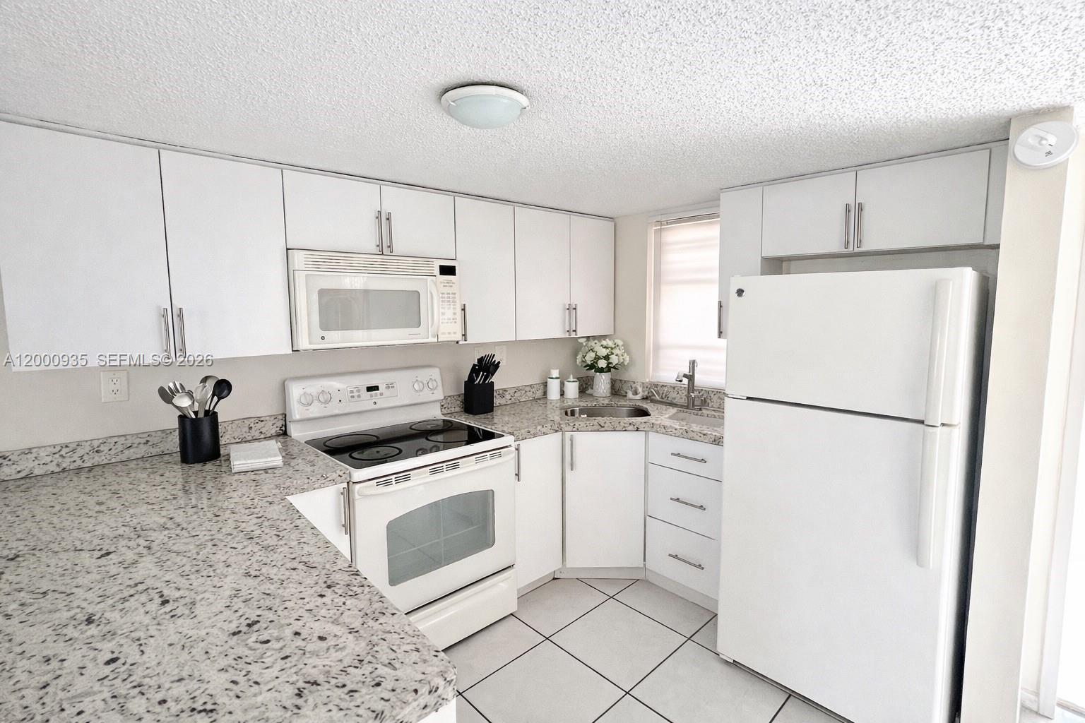 A white kitchen features granite countertops, white cabinetry, and a white appliance suite — 5575 W 26th Court # 203, Hialeah FL 33016, HIALEAH, FL