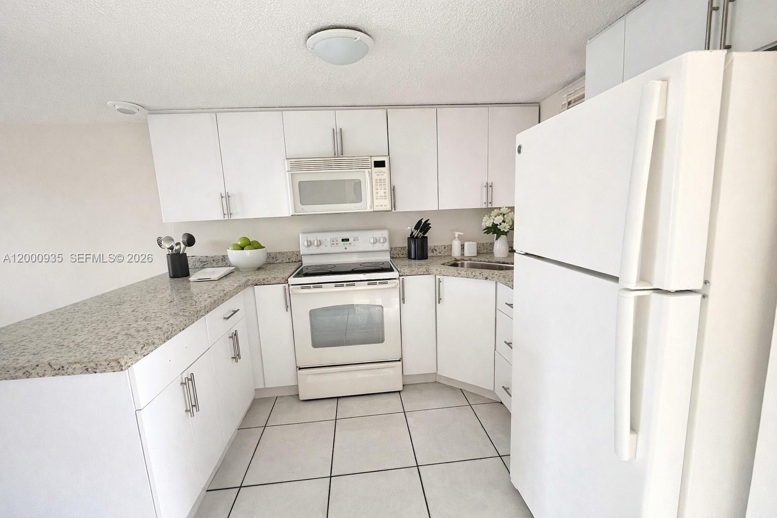 A white kitchen features granite countertops, white cabinetry, and a white refrigerator — 5575 W 26th Court # 203, Hialeah FL 33016, HIALEAH, FL