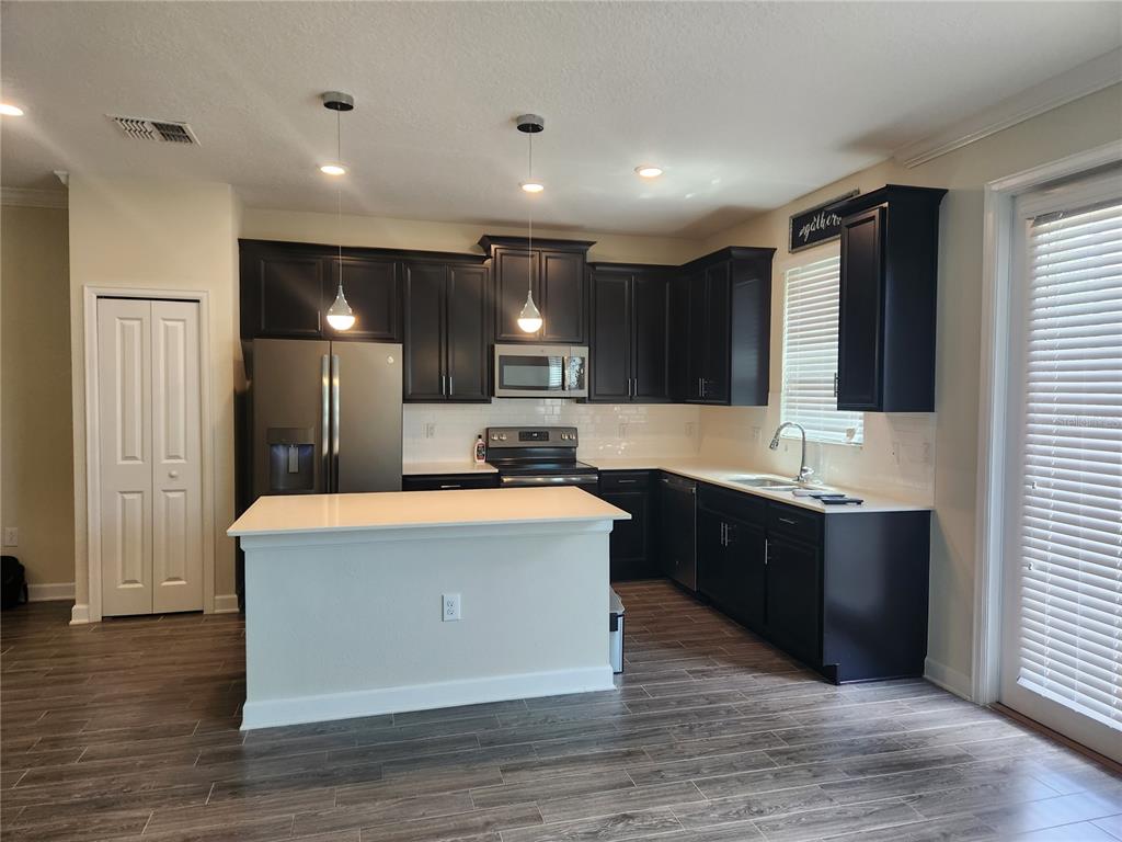 A kitchen features dark wood cabinets, stainless steel appliances, a white island, and wood-look flooring — 8506 ARCADIA LANE, DAVENPORT, FL