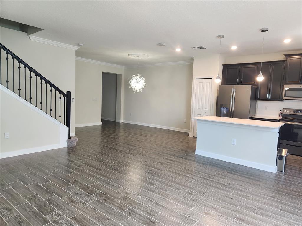 An open-concept kitchen and living area features wood-look tile flooring, dark cabinetry, and a staircase — 8506 ARCADIA LANE, DAVENPORT, FL