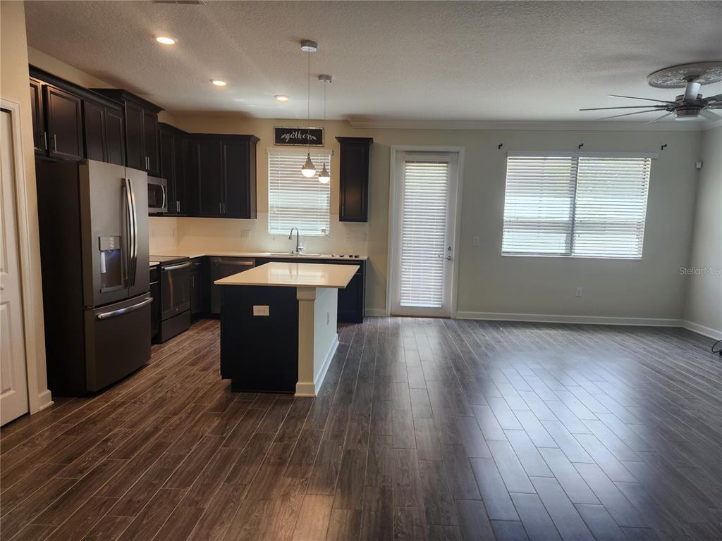 A kitchen with dark cabinets, a center island, and wood-look flooring opens to a living area — 8506 ARCADIA LANE, DAVENPORT, FL