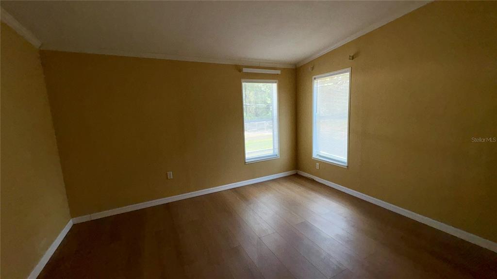 An empty room features mustard-colored walls, wood-look flooring, and two windows with white blinds — 19112 IVERSON ROAD, LUTZ, FL