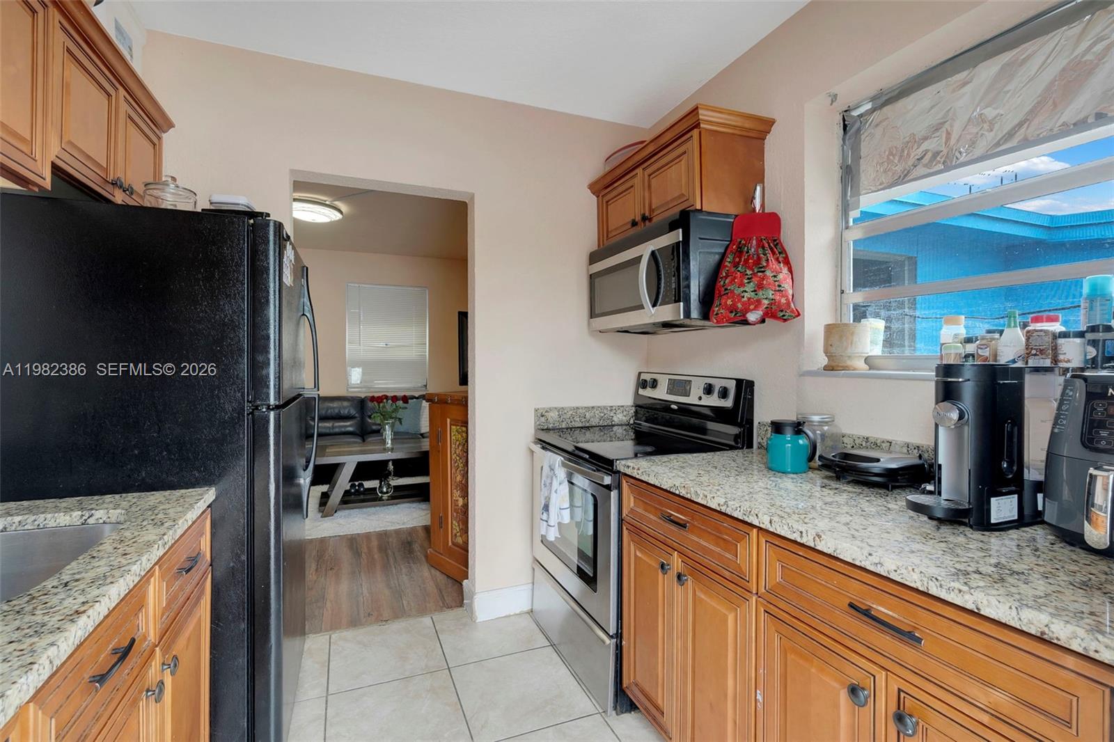 A kitchen features wood cabinets, granite countertops, stainless steel appliances, and a black refrigerator — 1449 NE 51st St, Pompano Beach FL 33064, POMPANO BEACH, FL