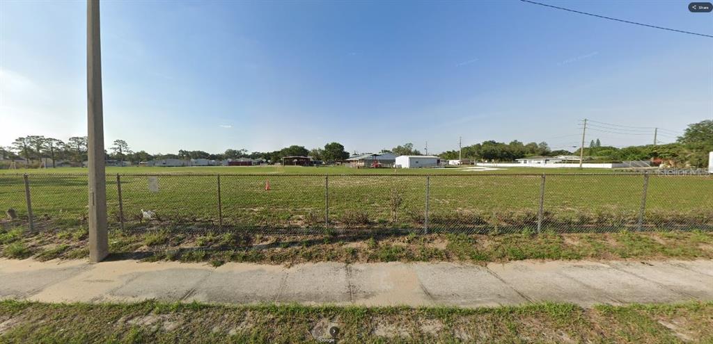 A chain-link fence encloses a large, flat, grassy vacant lot under a clear blue sky — HWY 60 E, LAKE WALES, FL