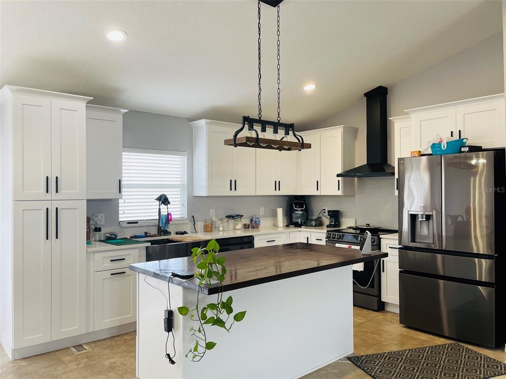 A kitchen features white cabinetry, a dark wood island countertop, and a black range hood — 346 PUFFER COURT, POINCIANA, FL