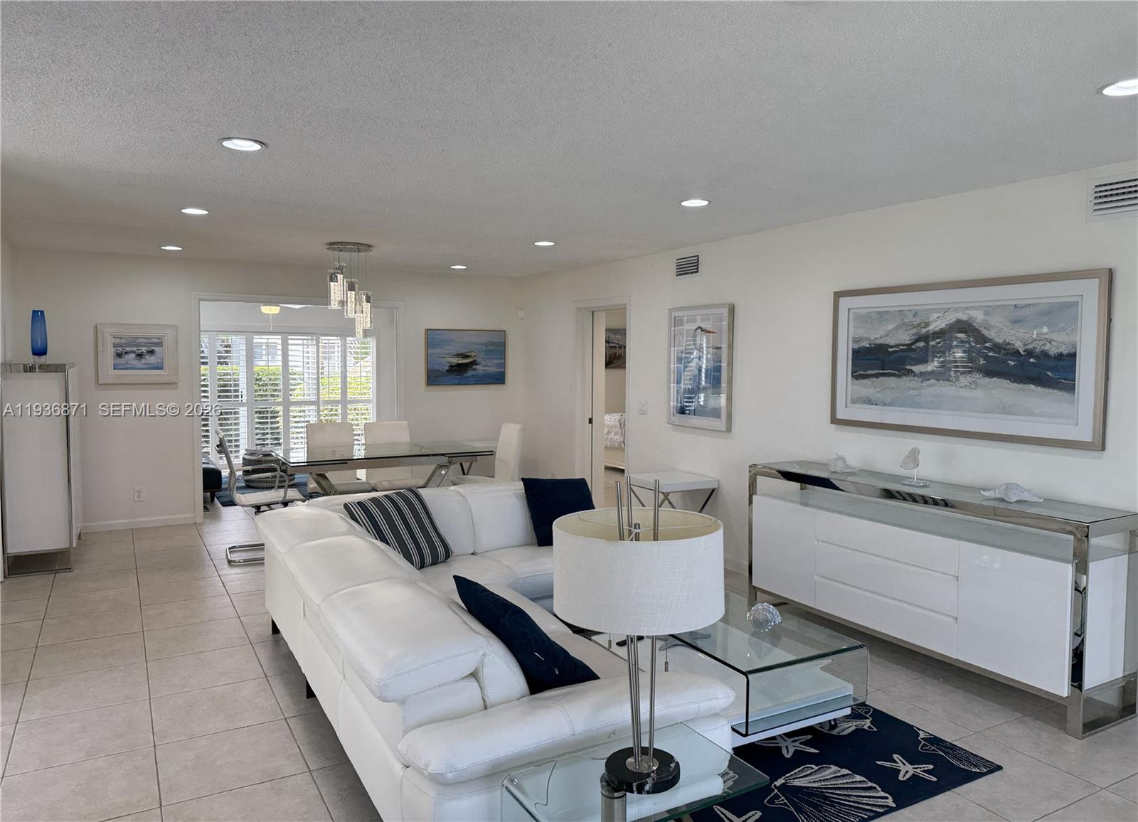 A living room features a white sectional sofa, glass coffee table, and coastal-themed wall art — 4161 S Us Highway 1 # K1, Jupiter FL 33477, JUPITER, FL