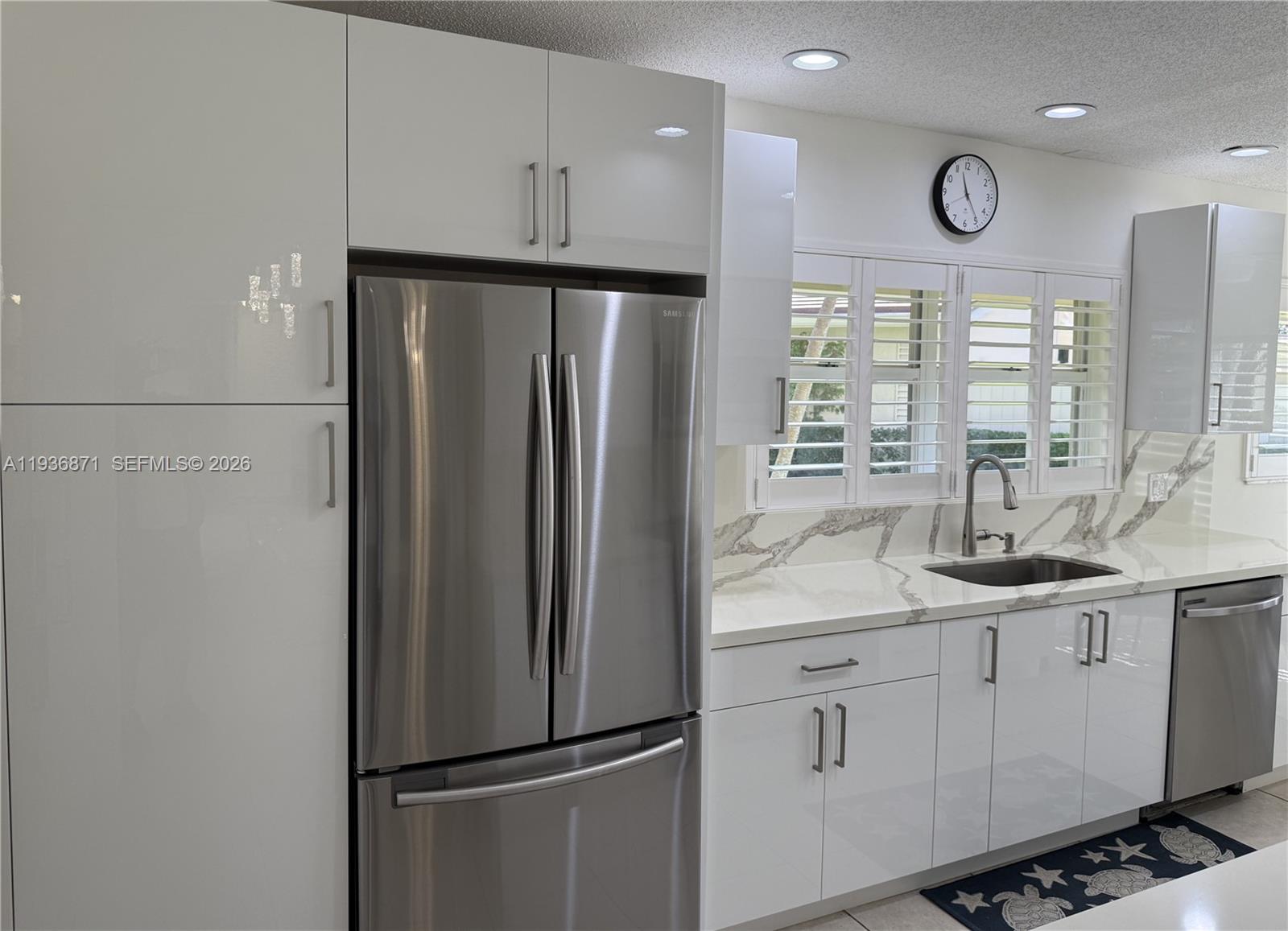 A modern kitchen features white high-gloss cabinets, stainless steel appliances, and marble-patterned countertops — 4161 S Us Highway 1 # K1, Jupiter FL 33477, JUPITER, FL