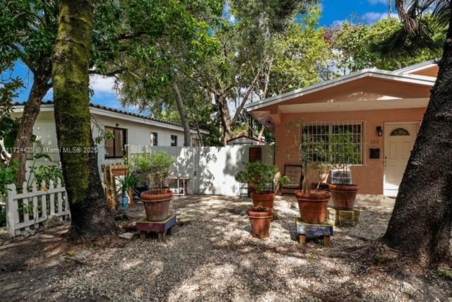 A gravel courtyard sits between two houses with potted plants and mature trees — 133 NE 48th St, Miami FL 33137, MIAMI, FL